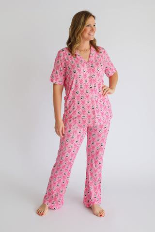 Woman wearing pink pajama set with ribbon and bow print, short sleeves, and flared pants.