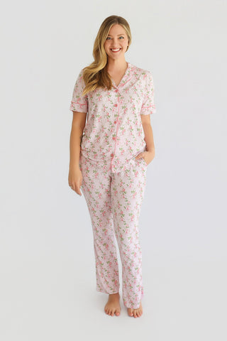 Woman wearing pink floral button-front pajama set with short sleeves and straight-leg pants.