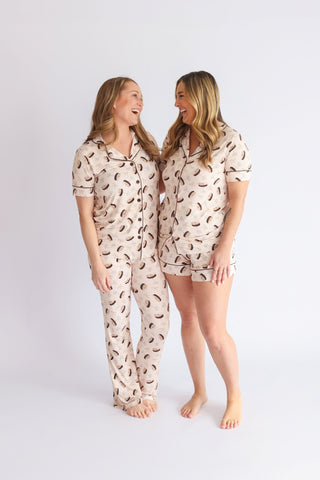 Two women wearing cream-colored pajama sets with martini glass print, one in full-length pants and one in shorts with short s