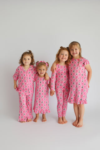Four young children wearing matching pink pajamas with sailboat and crown print patterns in various styles.