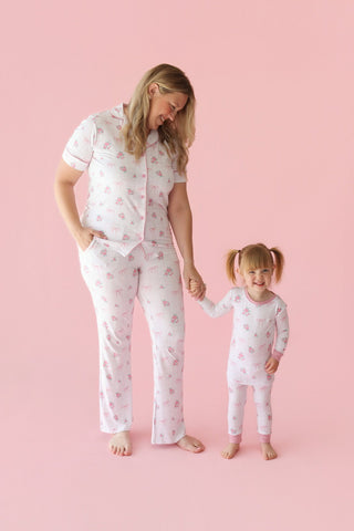 Woman and child wearing white pajama sets with pink rose and bow print on pink background.