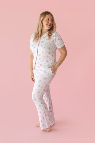 Woman wearing white short-sleeve pajama shirt and flare pants with pink rose and bow print.