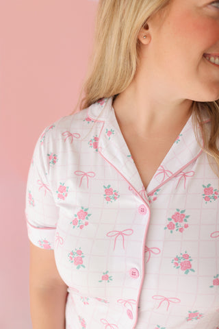 White short-sleeve pajama top with pink roses and bow pattern, pink button front, and piping trim.