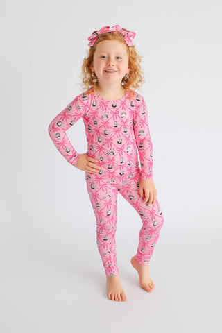 Child wearing pink ribbon bow hair clips on head with matching patterned pajamas.