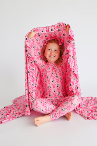 Child wearing pink pajamas with ribbon and ballerina print pattern, wrapped in matching blanket.
