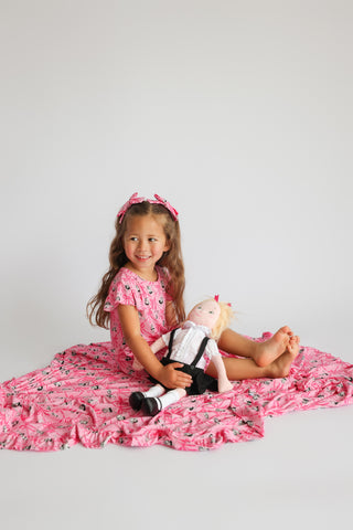 Pink ruffle blanket with small crown pattern, shown spread out with child and doll wearing matching outfits.
