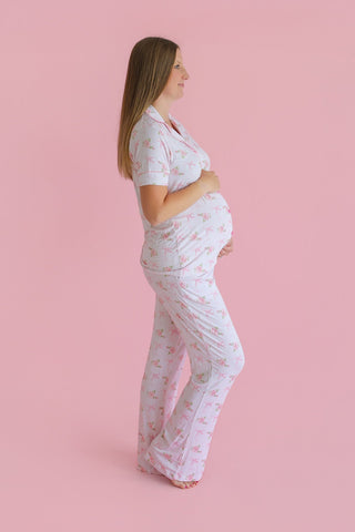 Woman wearing white short-sleeve top and flare pants with pink floral pattern against pink background.