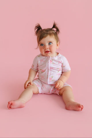 Infant wearing pink floral short-sleeve romper with button front and matching shorts against pink background.