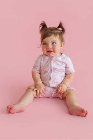Toddler wearing pink floral print short-sleeve romper with snap closure against pink background.