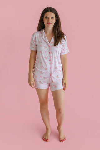Woman wearing white short pajama set with pink floral pattern and button-front shirt.