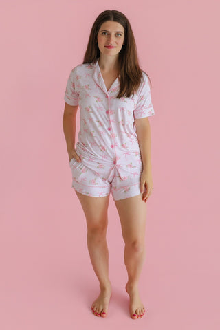 Woman wearing a white short-sleeved pajama set with pink floral print and button-front top paired with matching shorts.