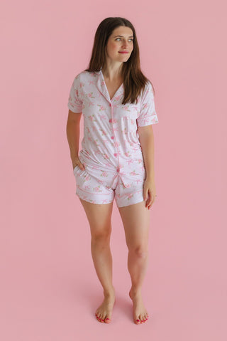 Woman wearing a white short-sleeved button-up pajama shirt and matching shorts with pink floral print.