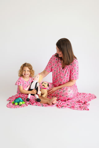 Woman and child wearing matching pink flare pajama sets with ribbon and bow print, holding stuffed animals.