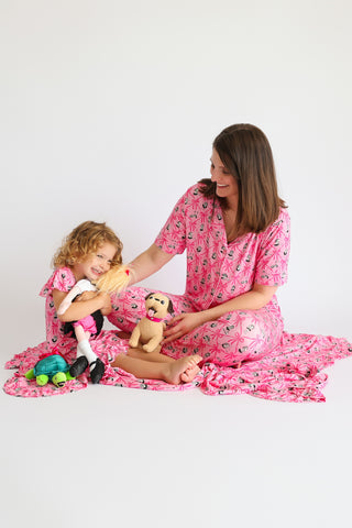 Woman and child wearing matching pink flare pajama sets with ribbon and bow print pattern.