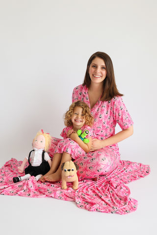 Woman and child wearing matching pink pajama sets with crown and heart pattern print, short sleeves, and flared pants.