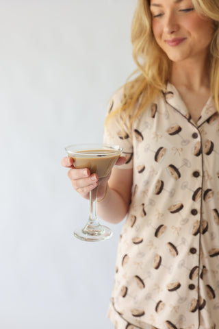Woman wearing cream pajama top with brown martini glass print, holding cocktail glass.