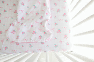 White quilted sleep sack with pink floral bunches and bow pattern displayed in crib.