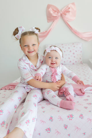 Pink and white floral bow hair clips worn by two children on a pink and white patterned bedding set.