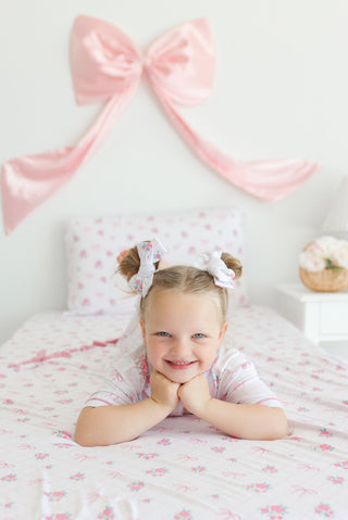 Two white hair clips with floral rose print worn by child in pigtails on bed with pink bedding.