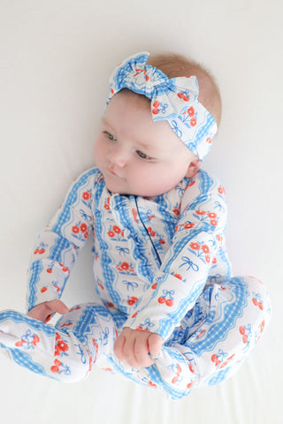 Infant wearing blue and white cherry-print romper with ruffled trim and matching bow headband.