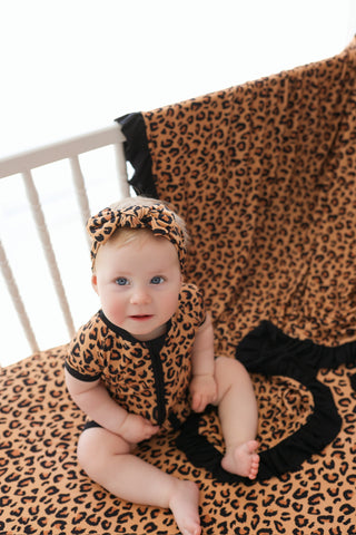 Infant wearing brown and black leopard print romper and matching headband, sitting on coordinating blanket.