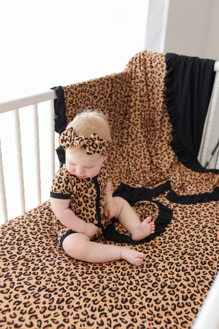 Infant wearing leopard print short-sleeved romper and matching headband, sitting on coordinating leopard print blanket.
