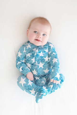 Infant wearing teal romper with white stars and moon pattern, front zip closure, long sleeves.