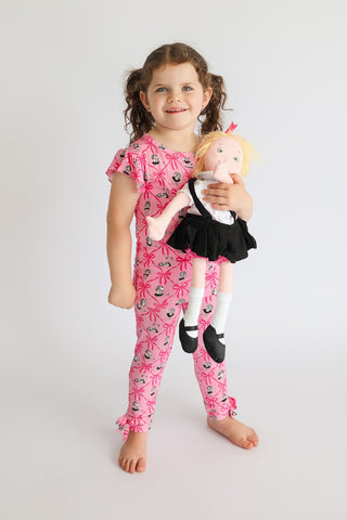 Child wearing pink sleep pants with ribbon and teacup print pattern, short-sleeved matching top.