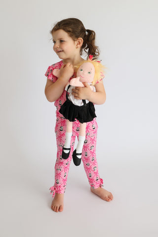 Girl wearing pink sleep pants with ribbon and teacup print, ruffled edges, and matching short-sleeved top.