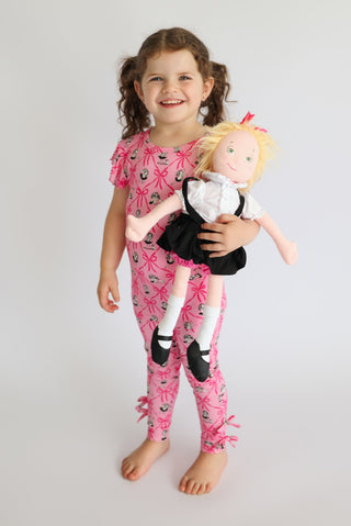 Child wearing pink sleep pants with ribbon bow and monkey print pattern, paired with matching short-sleeve top.