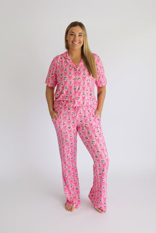 Woman wearing pink short-sleeve pajama set with ribbon and chandelier print, flare pants.