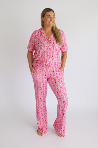 Woman wearing pink pajama set with ribbon and anchor pattern, short sleeves, and flare-leg pants.