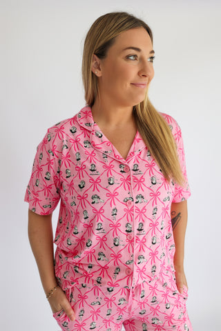 Woman wearing pink short-sleeve pajama top with ribbon bow and vintage girl print pattern.