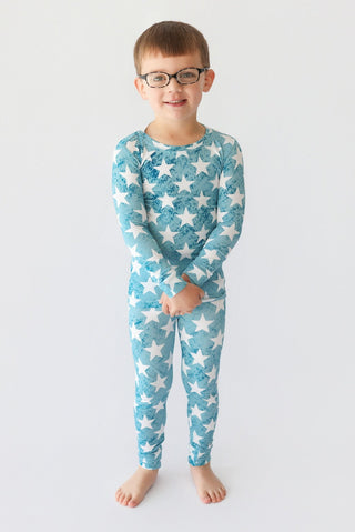 Child wearing turquoise two-piece pajama set with white star and textured pattern throughout.