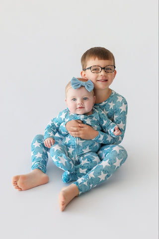 Two children wearing matching blue pajamas with white star pattern and coordinating hair bows.