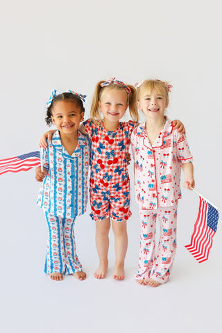 Three children wearing short sets with cherry, star, and flag patterns in red, white, and blue.