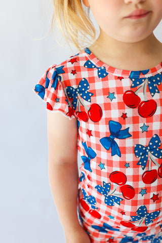 Child's short-sleeve top with red and white gingham pattern, red cherries, blue bows, and stars, featuring ruffled neckline a