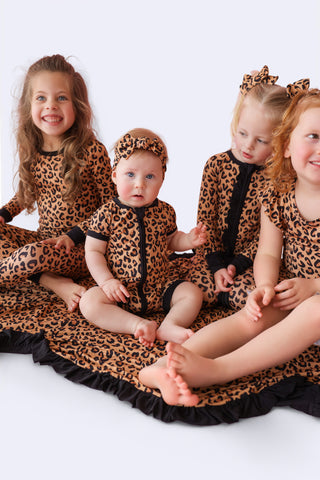 Children wearing leopard print rompers and matching headbands with black ruffled trim.