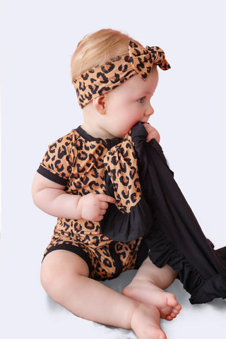 Infant wearing leopard print short-sleeve romper with matching headbow and black cape.