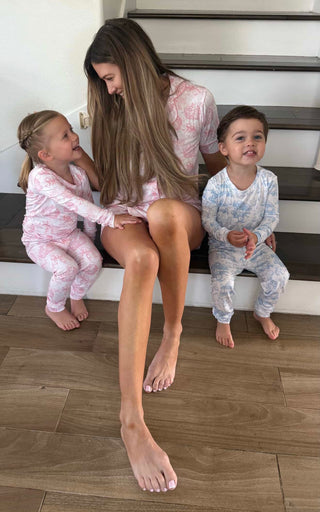 Woman and two toddlers sitting on stairs; woman wears pink toile pajama top, children wear matching toile pajama sets in pink