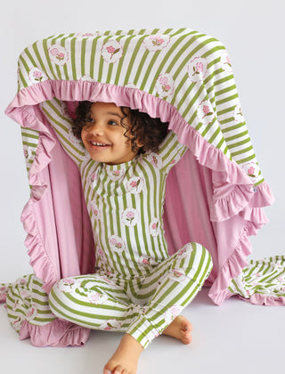 Toddler wearing green and white striped pajama set with pink floral details and matching ruffled blanket.