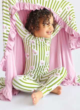 Toddler wearing green and white striped pajamas with floral print and pink ruffled blanket.