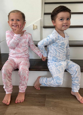 Two toddlers wearing long-sleeve toile print pajama sets in pink and blue bunny patterns sitting on stairs.