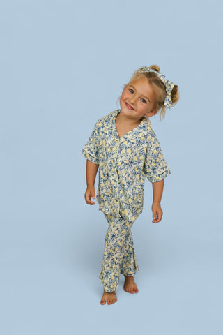 Girl wearing yellow and blue toile-printed short-sleeve shirt and flared pants with matching hair bow.