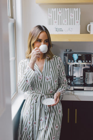 Woman wearing a striped robe with rose print and tie waist in cream and sage green.