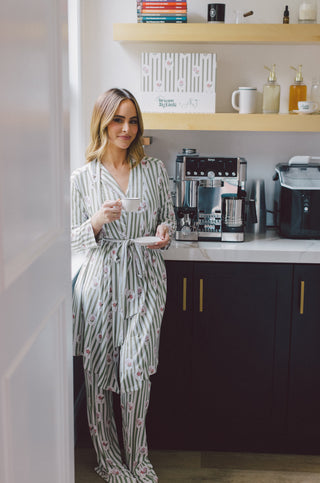 Woman wearing a striped robe with floral pattern, holding a mug in a kitchen setting.