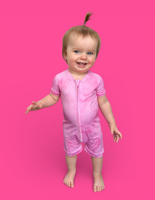Toddler wearing pink short-sleeved romper with front zip closure and striped trim on sleeves against pink background.