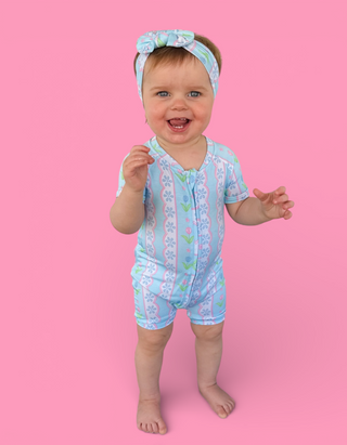 Toddler wearing light blue short-sleeved romper with tulip print and matching headband with bow.