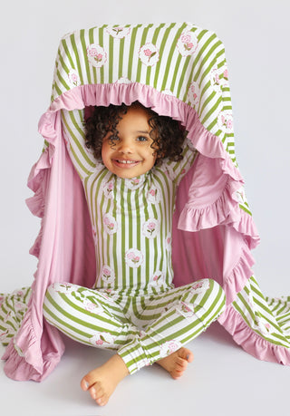Toddler wearing green and white striped pajamas with pink flower print and matching pink ruffled blanket.