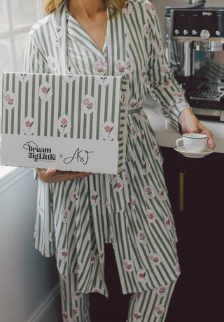 Person wearing green and white striped pajamas with floral print holding branded box while holding coffee cup.
